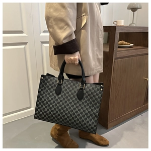 Detail of trendy M-patterned tote bag with leather handles and gold metal hardware