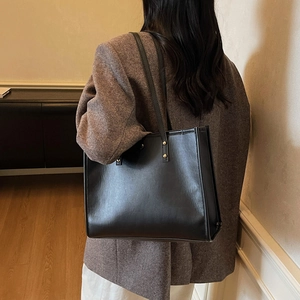 Classic black PU leather tote bag with gold hardware worn with a brown blazer jacket