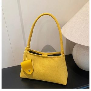 Détail du sac sous le bras jaune mat avec mini breloque devant une lampe douce
