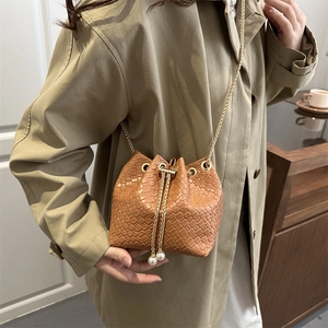 Brown woven bucket bag with gold chain strap and pearl charms on a model in a trench coat