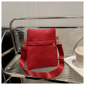 Detail of red lychee grain leather crossbody bag with golden zipper on a metal shelf