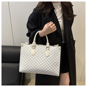 Detail of a large tote bag with M-pattern print and cream top handles on a model