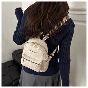 Détail de la texture en cuir tissé blanc et des ferrures dorées sur le mini sac à dos