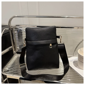 Detail of black pebbled leather crossbody bag with wide strap and gold hardware