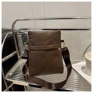 Detail of brown litchi pattern leather crossbody bag with wide nylon strap and gold hardware
