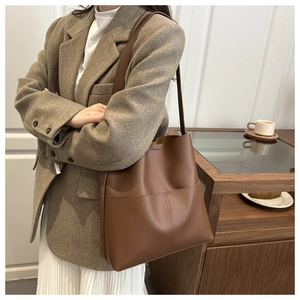 Detail of a large brown leather tote bag with vertical stitching shown on a model