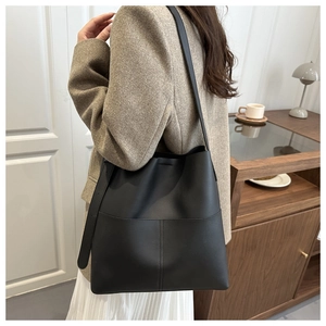 Detail of a large black leather bucket bag with decorative stitching on a model