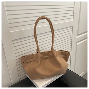 Detail of tan suede tote bag with long double handles and metal buckle on white books