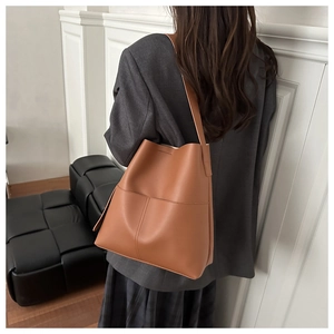 Detail of caramel brown leather bucket bag with wide strap on model back view