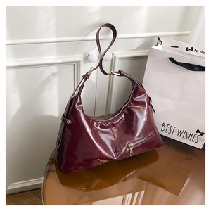 Detail einer burgunderroten glänzenden Hobo-Tasche mit goldfarbenen Metallteilen