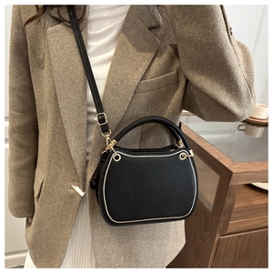 Detail of black crossbody bag with contrast piping and gold hardware on model
