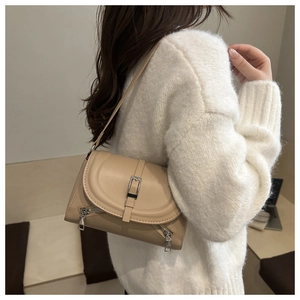 Detail of beige leather crossbody bag featuring silver side zippers and metallic buckle
