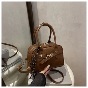 Detail of vintage brown leather Boston bag featuring woven tassel and metal bell charm