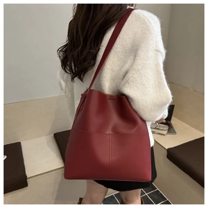 Detail of burgundy leather bucket bag with vertical stitching and slim shoulder straps