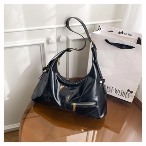 Detailansicht der schwarzen Lackleder-Hobo-Tasche mit goldenen Beschlägen auf dem Tisch