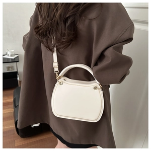 On-model view of a cream square crossbody bag with gold hardware and top handle