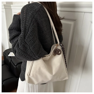 Detail of off-white tote bag with silk scarf and brown charm accessory on a model