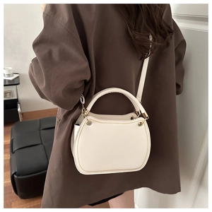 Close-up of creamy white minimalist crossbody bag with gold metal hardware on brown blazer