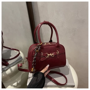 Close-up of burgundy leather crossbody bag with golden horsebit and braided charm