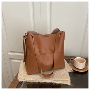 Detail of caramel brown leather tote bag on beige scarf with a cream ceramic cup