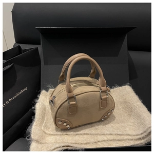 Detail of khaki suede mini bowling bag with silver studs on textured beige fabric