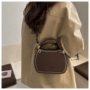 Detail of dark brown leather crossbody bag with cream contrast trim and gold hardware
