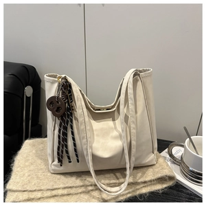 Detailed view of a cream large tote bag with brown woven pendant on a soft knit blanket