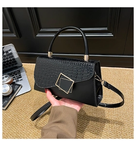 Detail of black crossbody bag with faux crocodile pattern and golden geometric buckle