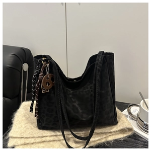 Detail of black leopard print tote bag with woven charm on soft beige texture