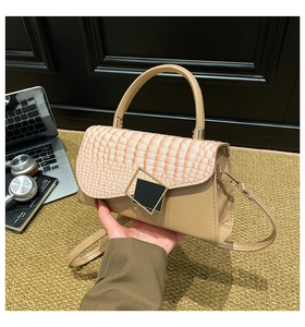 Detail of a beige crocodile-textured handbag with a gold geometric clasp and top handle