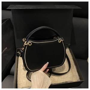 Detail view of a black square bag in gift box with gold stitching and hardware