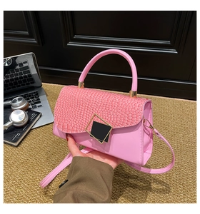 Detail of pink faux crocodile skin bag flap and gold geometric metal buckle in a workplace setting