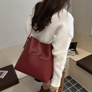 Chic burgundy leather tote bag with wide strap and front pocket in a minimalist style