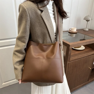 Brown leather bucket bag with cross stitching detail worn over the shoulder by a model