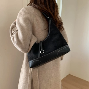 Minimalist black tote bag in mixed leather with white stitching worn by a woman