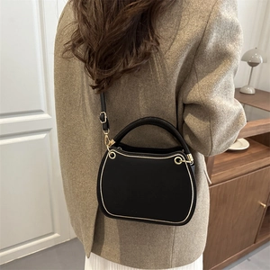 Chic black square crossbody bag with gold hardware shown on model in warm interior