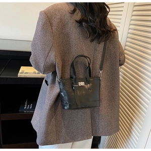 Détail du sac seau noir brillant avec fermoir rotatif argenté sur un blazer en laine