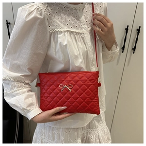 Detailed view of red quilted crossbody bag with gold bow clasp on white dress