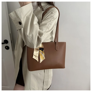Brown leather tote bag featuring contrast stitching and silk scarf on tan trench coat