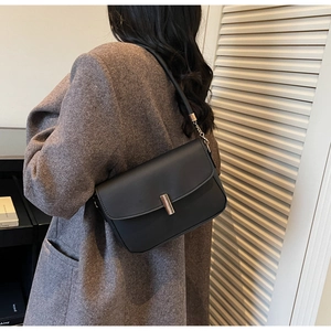 Detailed view of the sleek black crossbody bag with metallic clasp on a wool coat