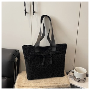 Detail of black tote bag with leopard print, woven handles and large capacity fabric texture