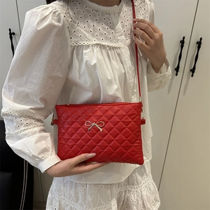Minimalist red quilted crossbody bag with metal bow accent and slim shoulder strap