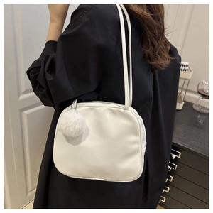 White minimalist square shoulder bag with plush pompom on model in modern interior