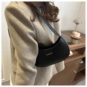 Detail of minimalist black half-moon shoulder bag with gold lettering in a cozy setting