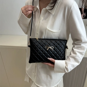 Minimalist black quilted crossbody bag with golden bow hardware and a slim leather strap