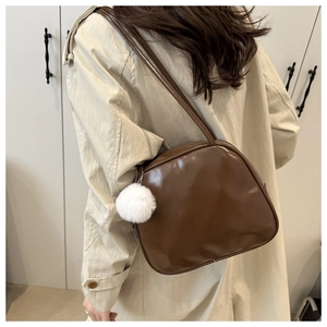 Detail of a dark brown glossy leather bag with a white fuzzy keychain ball pendant