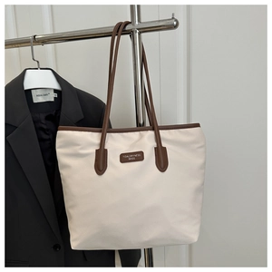 Detail of contrast color tote bag featuring premium leather logo tag and sturdy handles