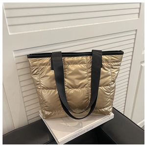 Detail of golden quilted tote bag with metallic finish and black woven strap handles
