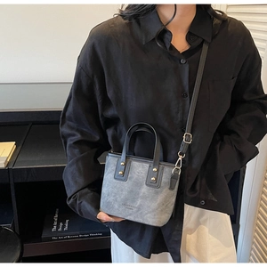 Detail of grey mini bucket bag with leather texture and black strap worn by model