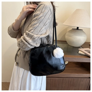 Detail of a black glossy patent leather shoulder bag with white plush ball charm